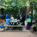 Einige Sängerinnen in einem grünen Innenhof an Holztischen