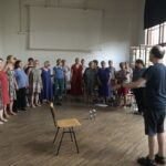 Probenfoto Hochsommer: Chor frontal, zu sehen außerdem einige Sprühflaschen, Getränke und die geöffneten Fenster
